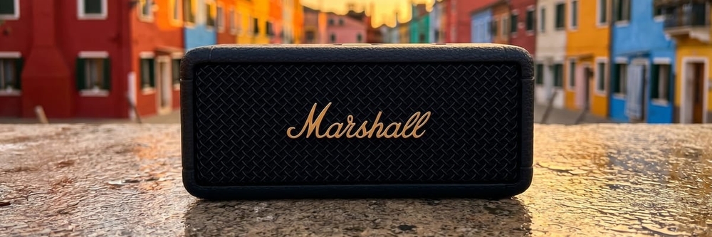 Marshall Emberton III portable speaker centered on a wet stone surface against colorful Burano canal houses at golden hour